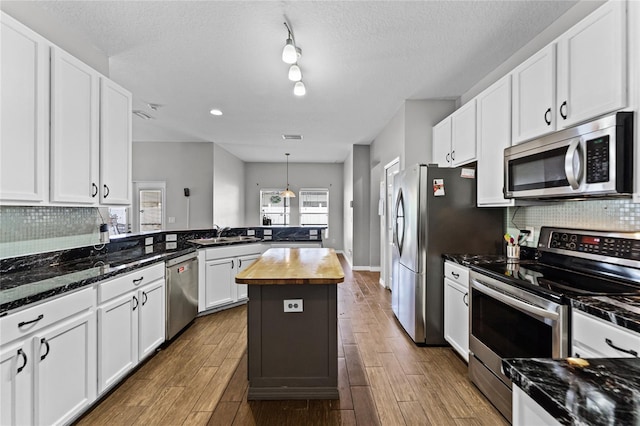 kitchen featuring wood finish floors, butcher block counters, backsplash, appliances with stainless steel finishes, and white cabinetry