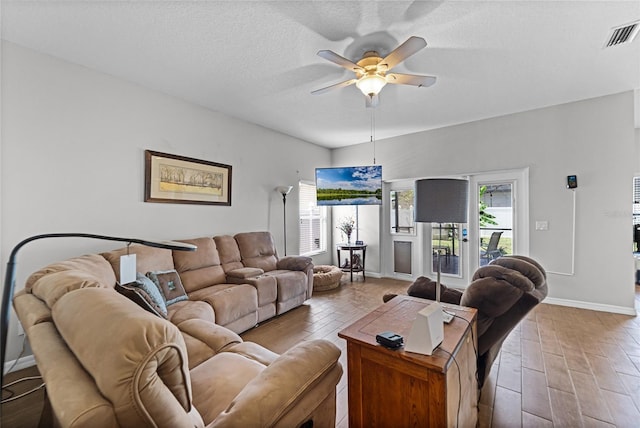 living area with light wood finished floors, visible vents, ceiling fan, a textured ceiling, and baseboards