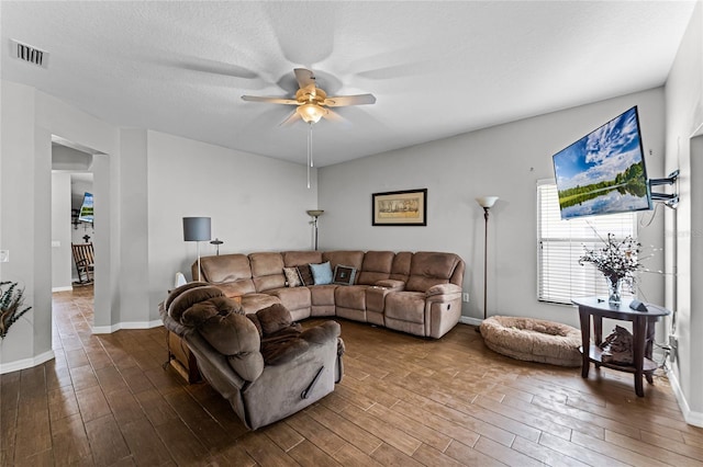 living room featuring a textured ceiling, wood finished floors, visible vents, baseboards, and a ceiling fan