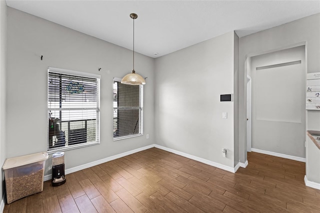 unfurnished dining area with baseboards and dark wood-type flooring