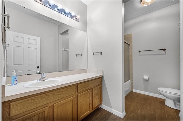 full bath with toilet, enclosed tub / shower combo, vanity, wood finished floors, and baseboards