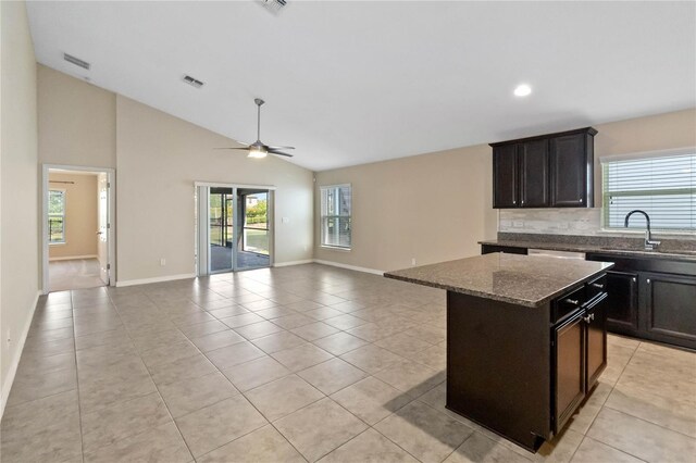 kitchen with ceiling fan, a center island, sink, dark stone countertops, and light tile patterned flooring