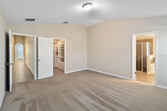 unfurnished bedroom featuring ensuite bathroom, a walk in closet, light carpet, and a closet