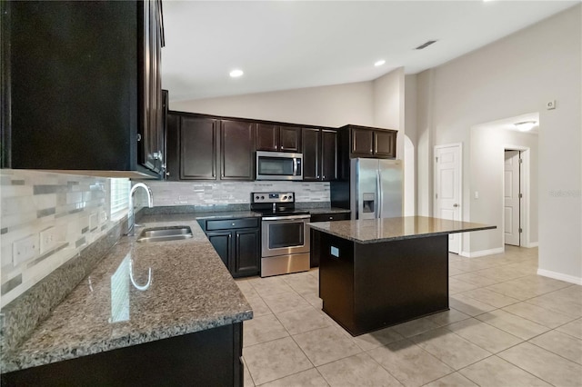 kitchen featuring stainless steel appliances, vaulted ceiling, sink, dark stone countertops, and a kitchen island