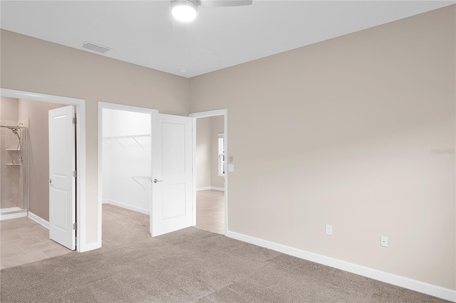 unfurnished bedroom featuring a walk in closet, a closet, ceiling fan, and light colored carpet