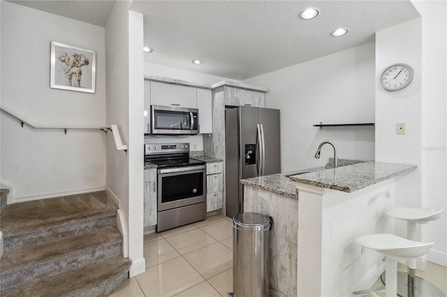 kitchen featuring kitchen peninsula, stainless steel appliances, white cabinets, light stone counters, and sink