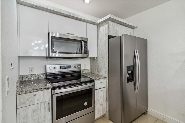 kitchen with light tile patterned floors, dark stone counters, stainless steel appliances, and white cabinetry