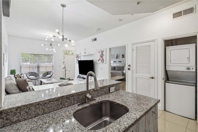 kitchen with pendant lighting, stacked washer / dryer, sink, a notable chandelier, and light tile patterned floors