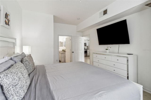 bedroom featuring connected bathroom and light hardwood / wood-style flooring