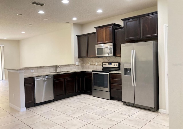 kitchen with kitchen peninsula, tasteful backsplash, light tile floors, sink, and appliances with stainless steel finishes