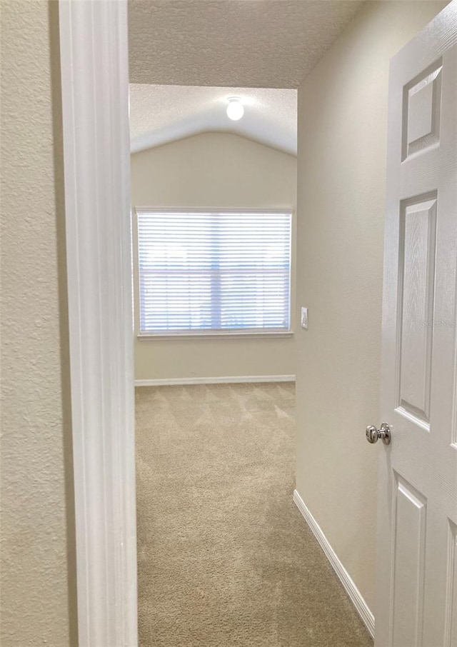 hallway with a textured ceiling, lofted ceiling, and carpet flooring