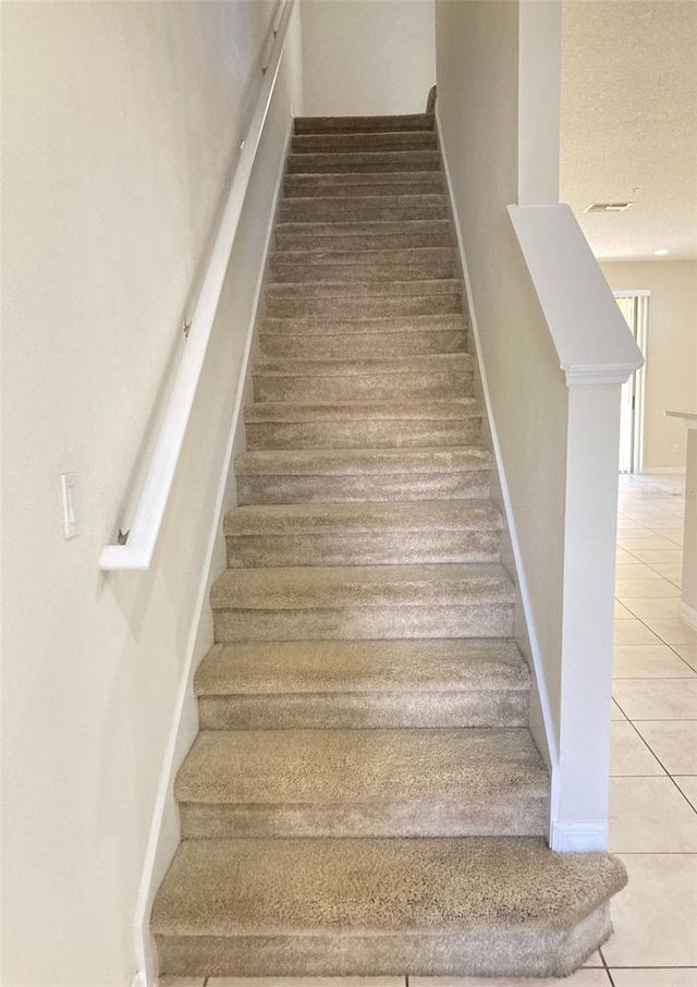 stairway with a textured ceiling and light tile floors