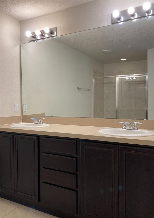 bathroom with a textured ceiling, tile flooring, a shower with shower door, oversized vanity, and dual sinks