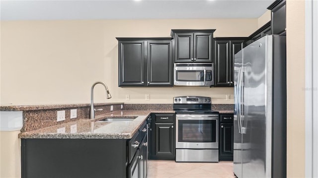 kitchen featuring dark stone counters, light tile patterned floors, sink, appliances with stainless steel finishes, and kitchen peninsula