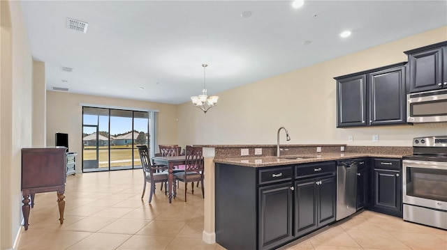 kitchen with appliances with stainless steel finishes, dark stone counters, sink, light tile patterned floors, and a chandelier