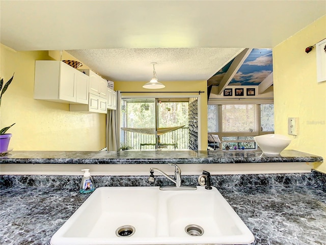 interior space featuring a textured ceiling, white cabinetry, sink, and hanging light fixtures