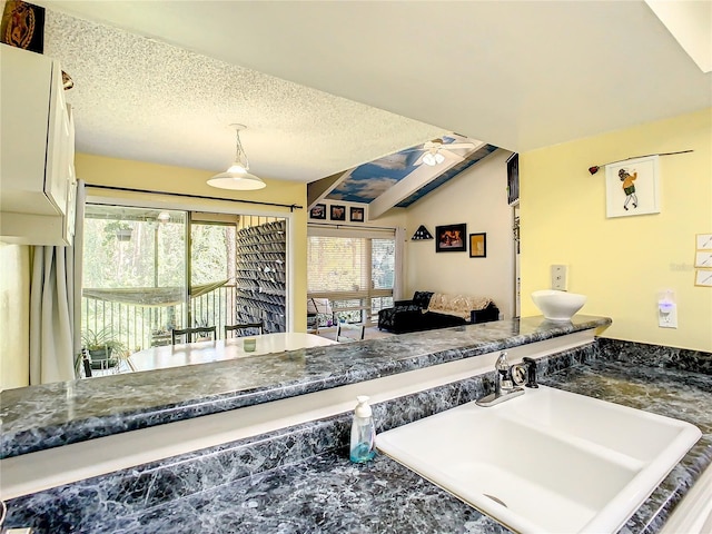 kitchen featuring lofted ceiling, sink, ceiling fan, a textured ceiling, and decorative light fixtures