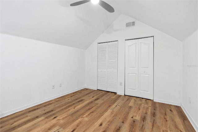 unfurnished bedroom featuring multiple closets, ceiling fan, vaulted ceiling, and light wood-type flooring