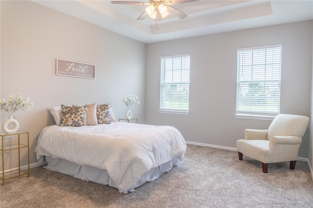 carpeted bedroom with ceiling fan and a raised ceiling