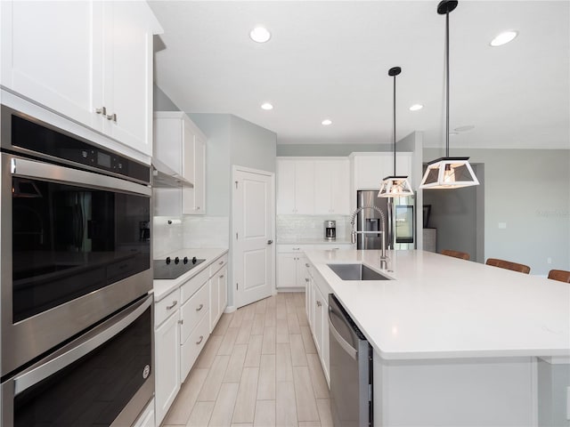 kitchen featuring a kitchen island with sink, stainless steel appliances, hanging light fixtures, and white cabinetry