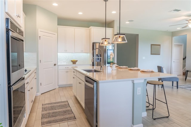 kitchen with pendant lighting, white cabinetry, a center island with sink, appliances with stainless steel finishes, and ceiling fan