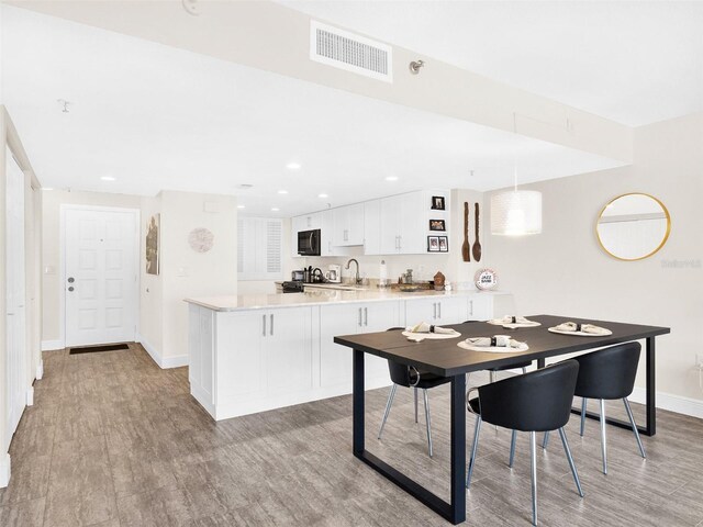 kitchen featuring decorative light fixtures, white cabinetry, light hardwood / wood-style floors, sink, and kitchen peninsula