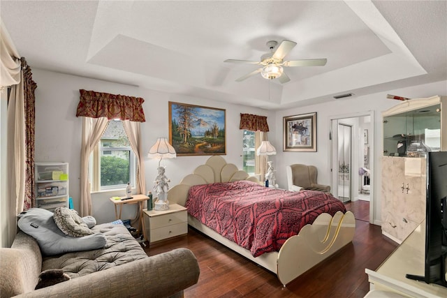 bedroom featuring ceiling fan, dark hardwood / wood-style flooring, and a tray ceiling