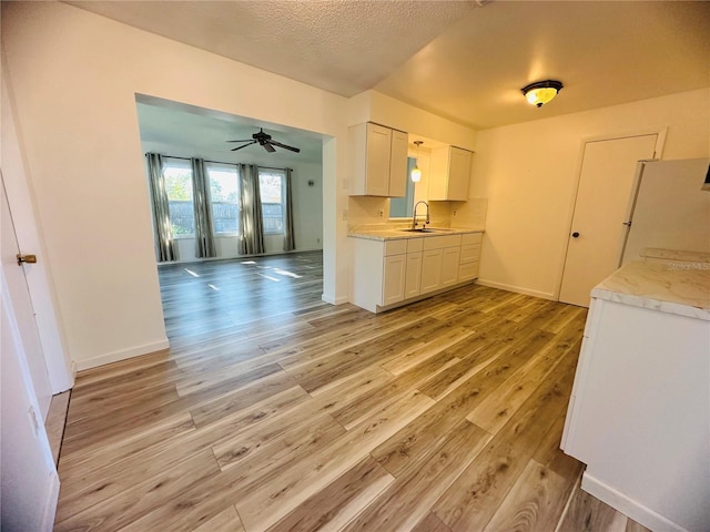 kitchen with ceiling fan, sink, white refrigerator, white cabinets, and light wood-type flooring