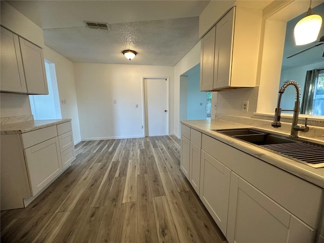 kitchen with decorative light fixtures, white cabinetry, light hardwood / wood-style floors, and sink