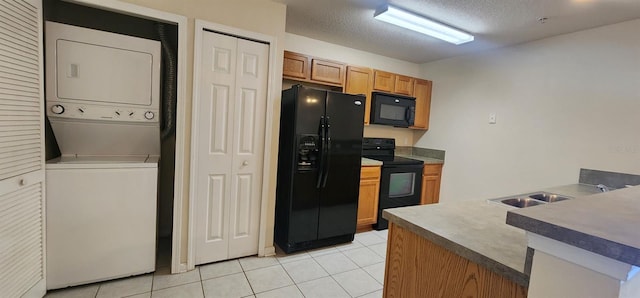 kitchen with stacked washing maching and dryer, light tile patterned flooring, black appliances, and a textured ceiling