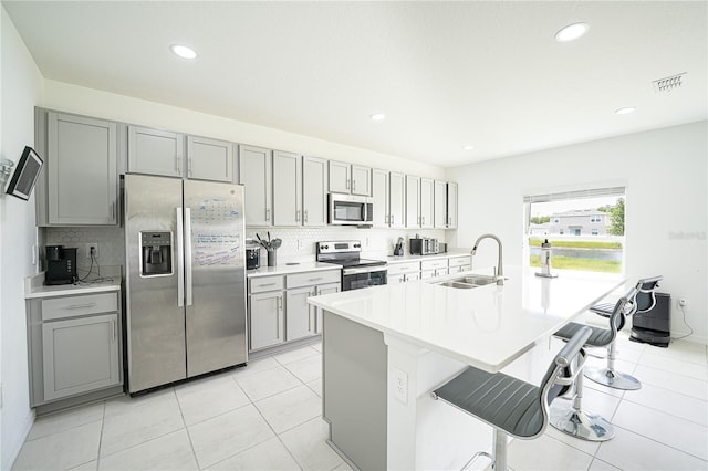 kitchen featuring stainless steel appliances, gray cabinets, backsplash, sink, and a kitchen bar