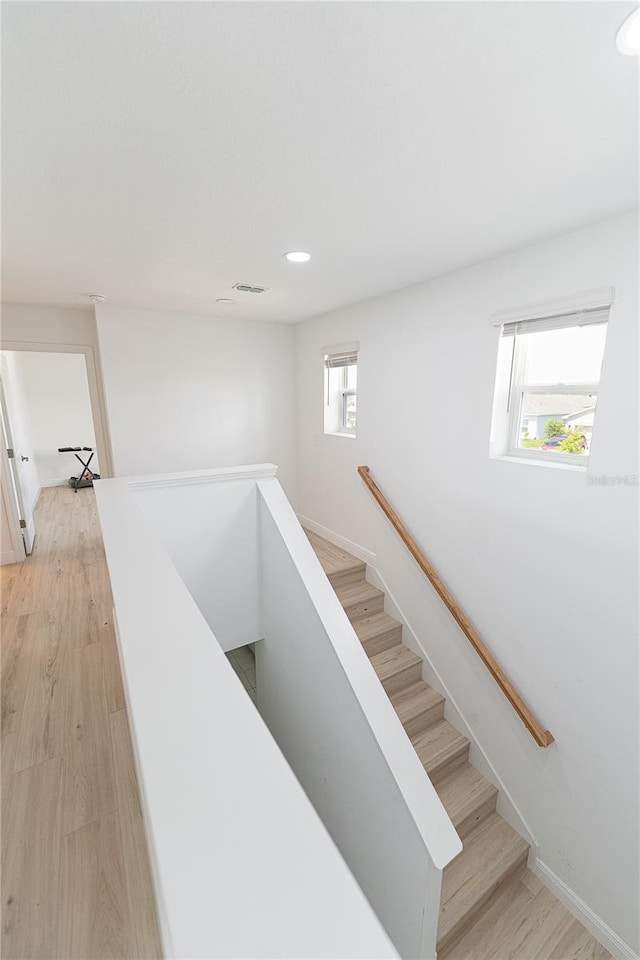 stairway with a wealth of natural light and light hardwood / wood-style flooring