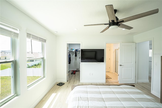 unfurnished bedroom with ceiling fan, a closet, a spacious closet, and light wood-type flooring