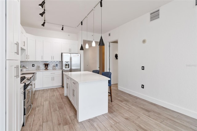 kitchen with white cabinetry, hanging light fixtures, backsplash, stainless steel appliances, and a center island