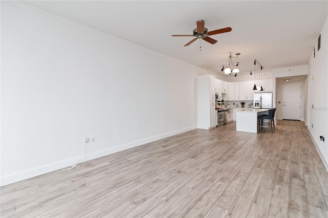 unfurnished living room with ceiling fan with notable chandelier and light hardwood / wood-style flooring