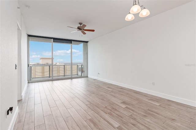 empty room with light hardwood / wood-style flooring, ceiling fan with notable chandelier, and a wall of windows