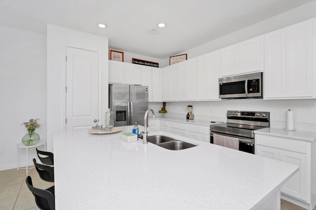 kitchen with white cabinets, light tile flooring, stainless steel appliances, a kitchen island with sink, and sink