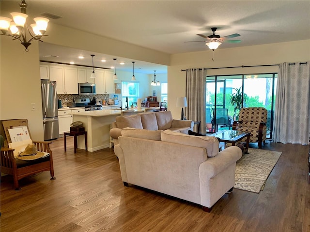 living room featuring dark hardwood / wood-style flooring, ceiling fan with notable chandelier, and a healthy amount of sunlight