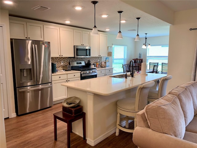 kitchen featuring appliances with stainless steel finishes, a center island with sink, decorative light fixtures, and a kitchen breakfast bar