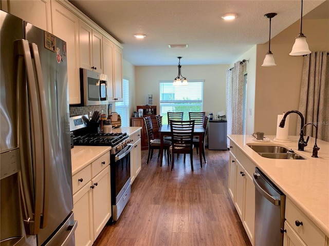 kitchen featuring appliances with stainless steel finishes, dark hardwood / wood-style flooring, sink, decorative light fixtures, and white cabinetry