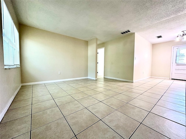 empty room featuring light tile patterned flooring, a notable chandelier, and a textured ceiling