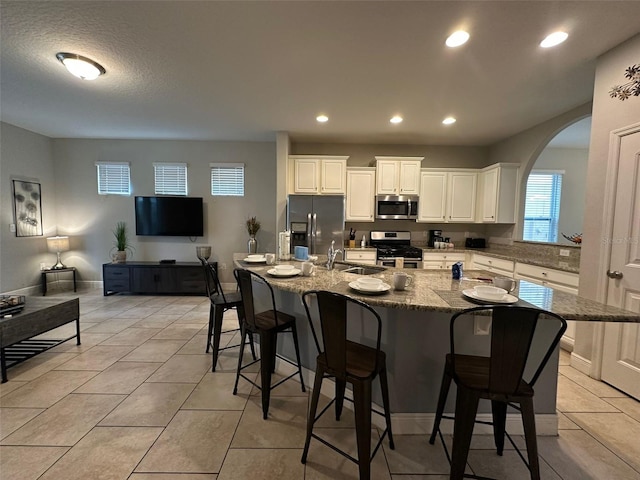 kitchen with sink, appliances with stainless steel finishes, a kitchen breakfast bar, stone counters, and a kitchen island with sink