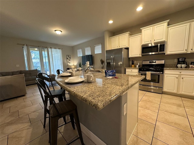 kitchen with white cabinetry, stainless steel appliances, and a center island with sink