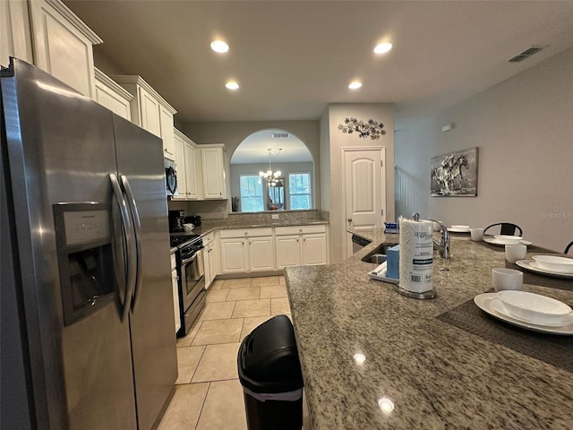 kitchen featuring light tile patterned floors, appliances with stainless steel finishes, white cabinetry, a notable chandelier, and dark stone counters