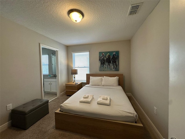 carpeted bedroom with ensuite bathroom and a textured ceiling