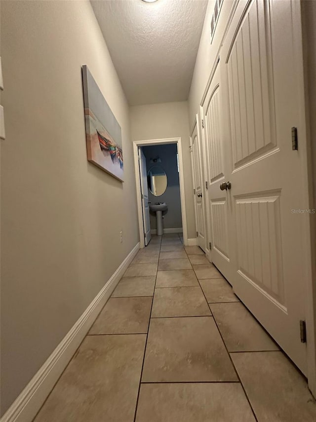 corridor featuring a textured ceiling and light tile patterned floors