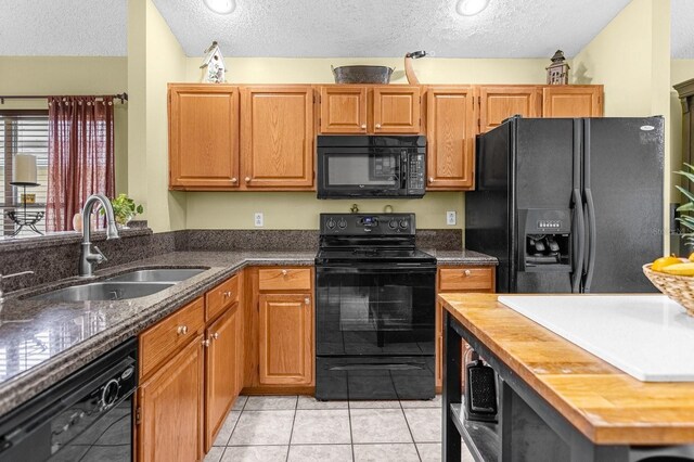 kitchen featuring a textured ceiling, light tile patterned floors, black appliances, butcher block countertops, and sink