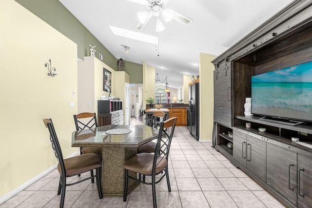 tiled dining space with sink, lofted ceiling with skylight, and ceiling fan