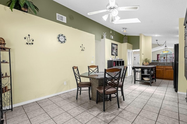 tiled dining room with ceiling fan and vaulted ceiling with skylight