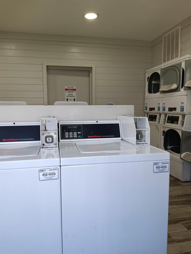 washroom featuring hardwood / wood-style flooring, stacked washer / dryer, wood walls, and washer and clothes dryer